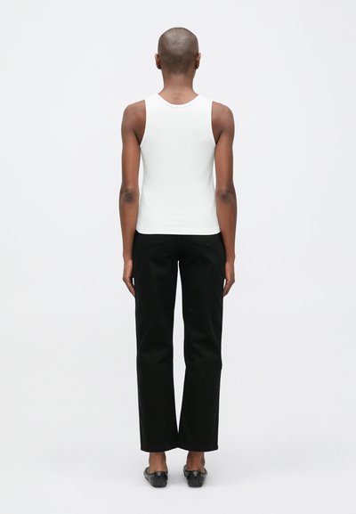 Baltas medvilnės marškinėlis be rankovių su prigludusia forma, derinamas su juodomis kelnėmis su aukštu juosmeniu, tiesiomis kojomis ir plokščiomis juodomis bateliais.