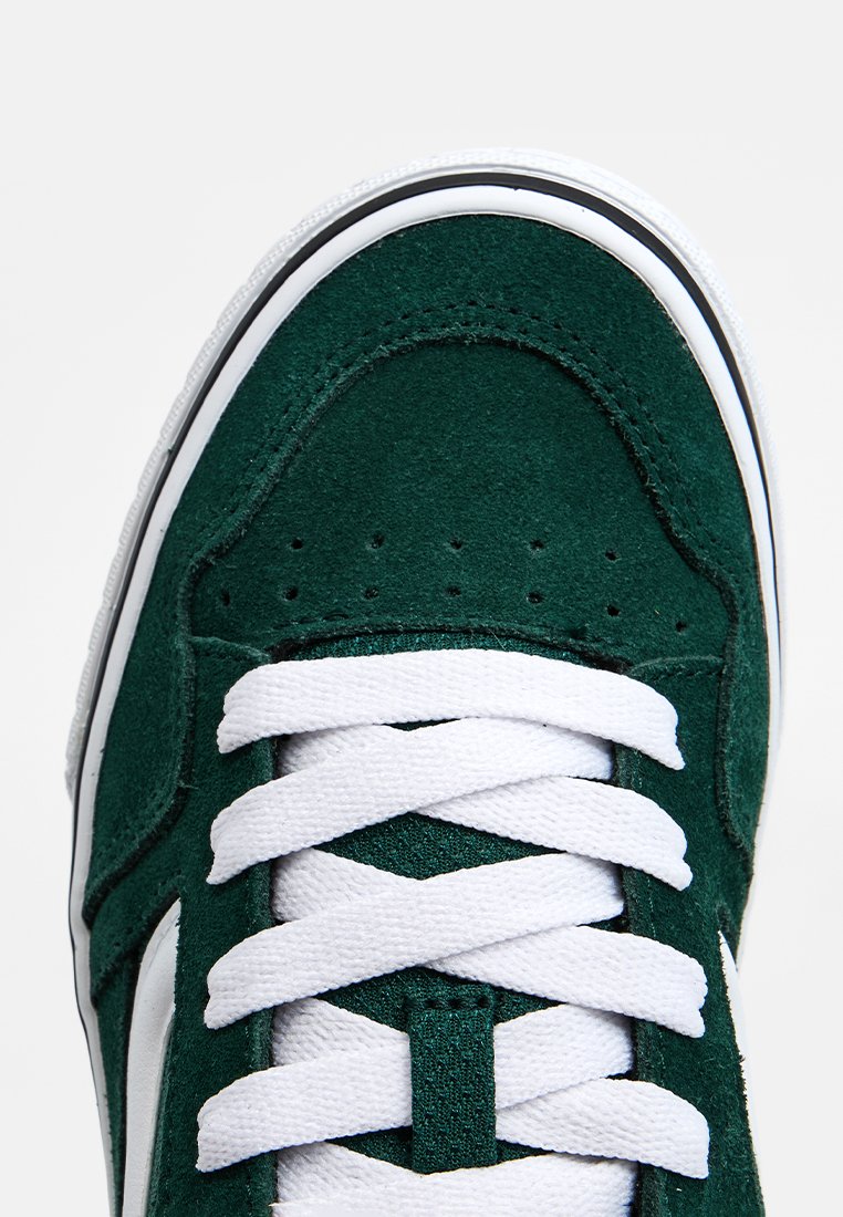 Baskets en daim vert avec des lacets blancs et une bande latérale blanche, présentant une surface texturée et un design à bout rond.