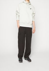 Ljusgrå hoodie med justerbara dragsnören och känguruficka, kombinerad med svarta cargobyxor med flera fickor och mörka sneakers.