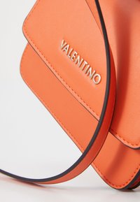 Borsa a tracolla in pelle arancione con superficie testurizzata, caratterizzata da un logo "VALENTINO" in argento e cuciture a contrasto nere.