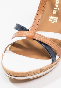 Sandale à bout ouvert avec des brides en cuir blanc, bleu marine et beige, dotée d'une semelle plateforme à texture liège et de détails surpiqués.