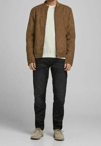 Hnědá suedová bunda s límcem, zapínáním na zip, v kombinaci s světlým svetrem, černými džíny a béžovými botami. Jednoduchý, moderní design.
