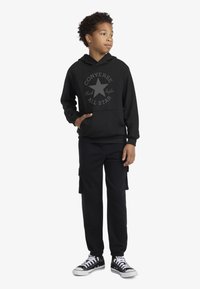 Hanorac negru cu buzunar frontal și logo gri "Converse All Star", asortat cu pantaloni cargo negri și adidași clasici negri cu alb.