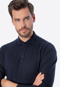 Dunkelblaues Langarm-Polohemd aus strukturiertem Stoff, mit drei Knöpfen und einem klassischen Kragen. Figurbetonter Schnitt, minimalistischer Stil.