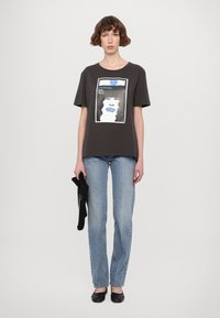 Grijze katoenen t-shirt met een grafische print van een gezicht met blauwe accenten, gecombineerd met lichtblauwe jeans en zwarte ballerina's.