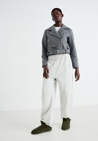 Veste biker en mélange de laine gris avec fermetures éclair argentées, taille ceinturée, associée à un pantalon de survêtement gris léger et des bottines vert olive.