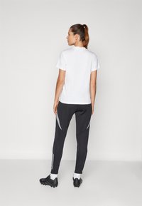 White short-sleeve t-shirt paired with dark gray sweatpants featuring silver accents and stripes, and black athletic shoes with white socks.