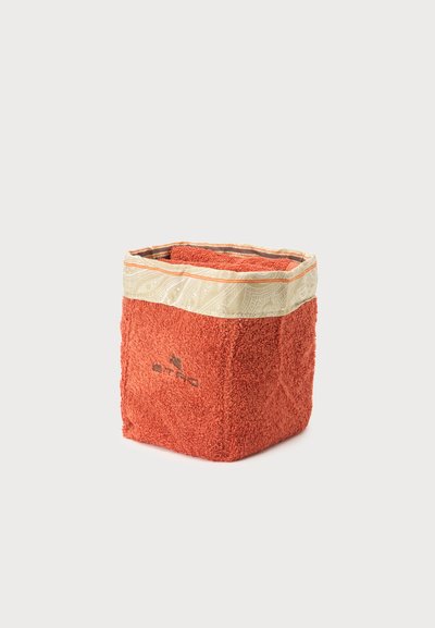 Panier de rangement carré en tissu avec côtés en éponge couleur rouille et bordure en tissu beige à motifs, plié à l’intérieur sur un fond uni.