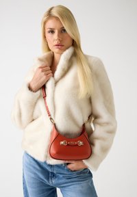 Witte jas van nepbont over casual blauwe spijkerbroek, met een kleine rode leren handtas met gouden hardware en een gebogen ontwerp.