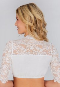 Weißes Cropped-Top mit langen Spitzenärmel und tailliertem Oberteil mit gerafftem Saum. Die Spitze hat florale Muster und sorgt für zusätzlichen Textur.