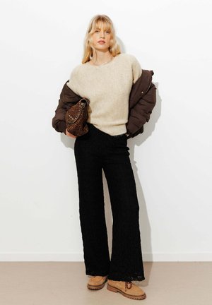 Pull beige texturé, doudoune marron, pantalon large noir, chaussures couleur sable et sac à imprimé animal marron. Fond minimaliste.