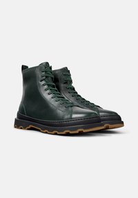 Botines de cuero verde hasta el tobillo con cordones, punta redonda, suela de goma negra gruesa y suela de goma en contraste. Textura suave con un diseño minimalista.