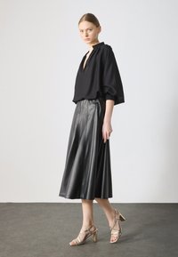Black oversized blouse with a V-neck, paired with a high-waisted, pleated black leather skirt. Features strappy metallic heels.