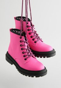 Stivaletti alla caviglia in pelle rosa con suole in gomma nere, dotati di lacci a motivo nero e rosa e una finitura liscia. Suola spessa per una buona trazione.