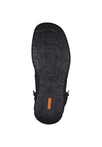 Schwarze Gummisohle mit strukturierten, gemusterten Rillen für Grip; mit einem auffälligen orangen Logo und verstärkten Kanten für Langlebigkeit.