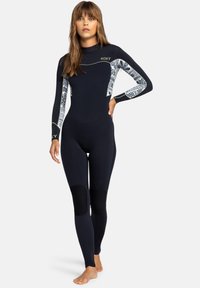 Combinaison de plongée noire à manches longues et genouillères, avec des accents à motifs contrastés en blanc. Comprend un col haut et un design ajusté.