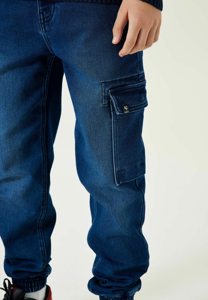 Dunkelblaue Cargo-Hose aus Denim, mit einer Seitentasche, elastischen Bündchen und einer glatten Textur, mit einem kleinen sichtbaren Markenlogo.