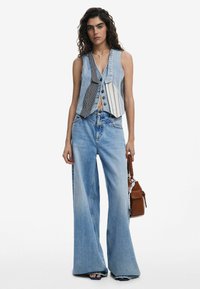 Chaleco de mezclilla con un diseño de patchwork y botones, combinado con jeans de pierna ancha en un tono azul desvanecido. También incluye un bolso marrón.