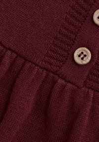 Burgunderfarbiges Strickkleid mit einem strukturierten Muster, einer gerafften Rüsche und zwei hellen, runden Knöpfen, die prominent zur Geltung kommen.