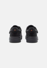 Un paio di sneakers nere con piccole borchie e suole spesse, viste da dietro su uno sfondo bianco.