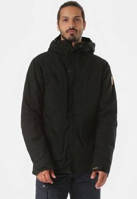 Sort vandtæt jakke med hætte, der har en frontlynlås, trykknapper og en diskret logo på kanten. Glat, holdbart stof.