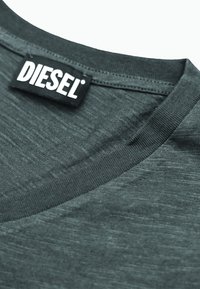 Primo piano di un tessuto grigio scuro con scollatura a costine e un'etichetta nera cucita nel colletto, etichettata "DIESEL".