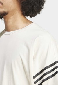 Kortärmad creamfärgad t-shirt i mjukt tyg, med rundad halslinning och tre svarta horisontella ränder på vänster ärm.