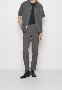 Grijs denim overhemd met korte mouwen over een zwart T-shirt, gecombineerd met grijze, op maat gemaakte broek en zwarte leren enkellaarzen. Details omvatten een zak en structuur.