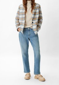 Blazer a cuadros en beige y azul, suéter de punto crema, jeans rectos azul claro y zapatos sin cordones beige con suela texturizada.