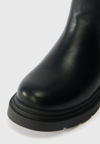 Črne usnjene gležnjarje z zaobljenim prstom in debelim gumijastim podplatom, ki se odlikujejo po gladki teksturi in minimalisitičnem oblikovanju.