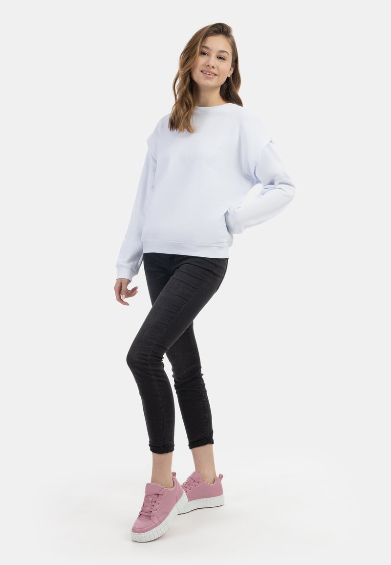 Witte sweatshirt met lange mouwen, gecombineerd met zwarte skinny jeans en roze sneakers. De outfit heeft een casual, ontspannen pasvorm.