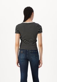 Un haut à manches courtes rayé noir et blanc associé à un jean bleu foncé avec des poches arrières et un petit logo sur la taille.