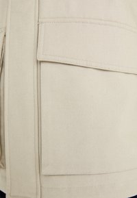 Primer plano de una tela de lienzo beige que presenta un gran bolsillo parche con bordes cosidos, textura suave y superficie uniforme.