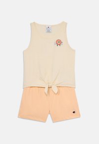 Top giallo chiaro senza maniche con una vita annodata e una grafica floreale colorata. Abbinato a pantaloni corti in pesco morbido, entrambi in cotone.