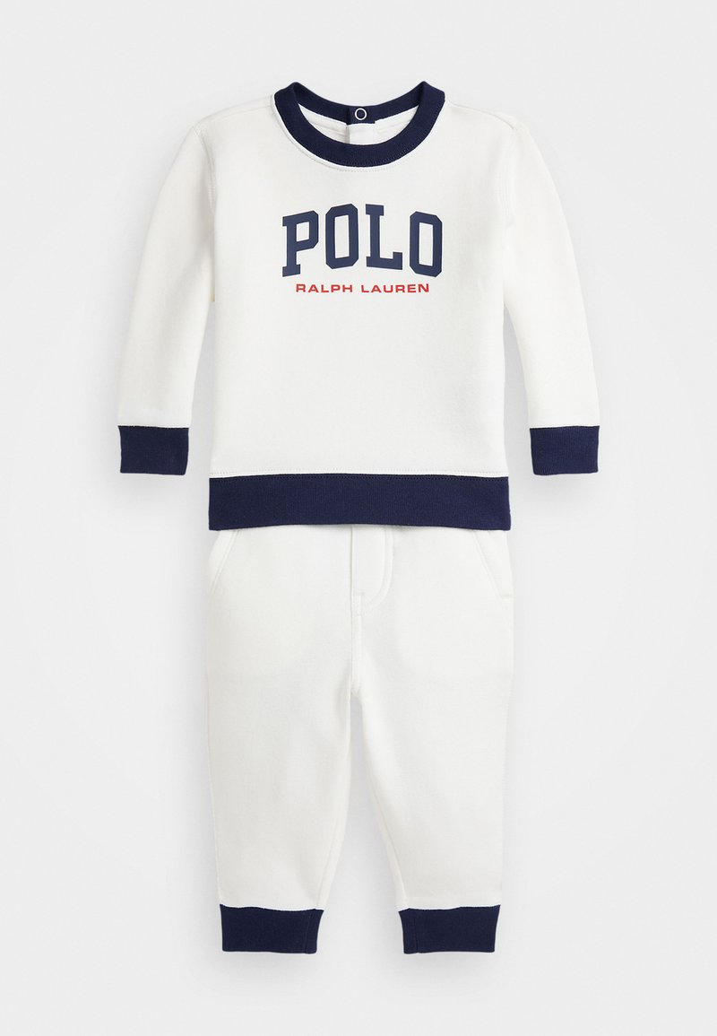 Fehér pulóver tengerészkék részletekkel, a "POLO RALPH LAUREN" felirattal vastag betűkkel. Együtt viselve a passzoló fehér melegítőnadrággal, szintén tengerészkék díszítéssel.