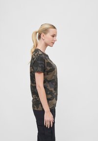 Kamo-mønstret kortermet t-skjorte i grønn, brun og marineblå, laget av mykt stoff med klassisk rund hals, båret med svarte cargo-bukser.