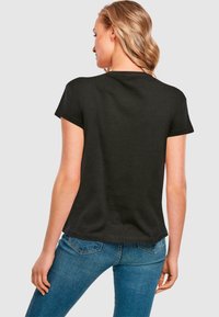 Black cotton t-shirt with short sleeves, relaxed fit, and curved hem, paired with blue jeans. No visible patterns or accents noted.