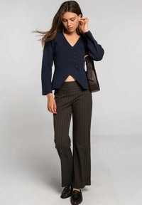 Pull en tricot côtelé marine avec un col en V et trois boutons, associé à un pantalon à rayures marron évasé et des mocassins noirs.