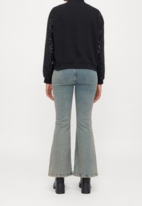 Czarna kurtka z cekinowymi rękawami, zestawiona z jasnoniebieskimi dzwonami. Widok od tyłu ukazuje prążkowany dół i dopasowaną sylwetkę. Czarne botki na obcasie.