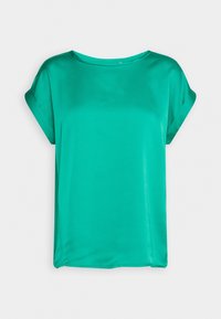 Blouse courte à manches courtes bleu sarcelle vif avec un col rond et des manches légèrement retroussées, présentée sur un fond blanc uni.