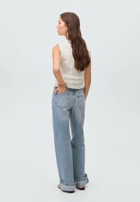 Haut blanc à volants avec un col haut, associé à un jean large bleu clair. Le modèle de dos montre une texture douce et une coupe décontractée.