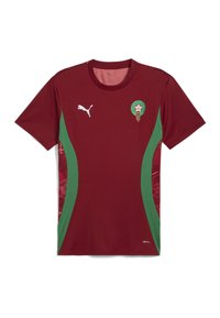 Maroonin värinen jalkapallo-asu, jossa on vihreät sivupaneelit, pyöreä kaula-aukko, Puma-logo ja ympyränmuotoinen marokkolainen emblem rinnan kohdalla. Pinta on teksturoitu.