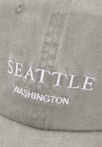 Grijze corduroy pet met witte geborduurde tekst: "SEATTLE" en "WASHINGTON." Het heeft een ronde kroon en een gestructureerd oppervlak.