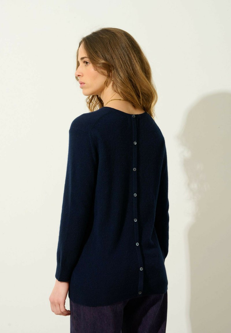 Granatowy sweter wykonany z miękkiego materiału, z długimi rękawami, okrągłym dekoltem i detalem z zapięciem na guziki z tyłu.