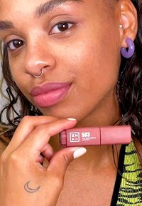 Långvarigt läppstift i ett rektangulärt rör, med en rosabrun nyans, och vit text på sidan som anger nyansen "503." En person håller i röret.