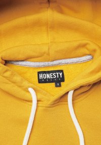 Yellow hoodie made of soft fabric, featuring a gray interior lining, white drawstrings, and a black label displaying “HONESTY RULES,” size S.
