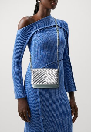 Borsa a tracolla con motivo a zigzag argento e tracolla azzurro chiaro, esposta su un vestito blu a coste con design off-shoulder.