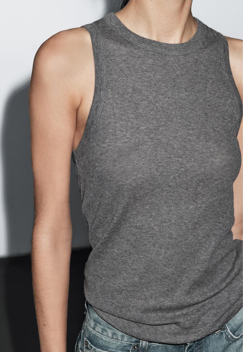 Gray sleeveless top made of soft cotton, featuring a round neckline and a fitted design, paired with blue denim jeans.
