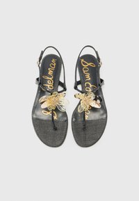 Sorte slingback-sandaler med teksturert overflate, med en klar blomstermotiv og gulllogo på innersålen. Flat såledesign.