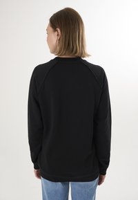 Must värviline kaua varrukatega dressipluus, millel on ümmargune kaelus, ribakujulised mansetid ja tagumised raglan õmblused. Sile kangatekstuur. Kanda helesiniste teksadega.